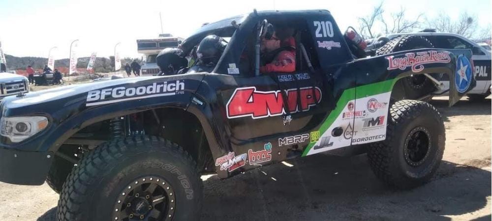 Ted Moncure driving a black off-road racing truck number 210, marked with BFGoodrich and 4WP decals, parked on a dirt lot.
