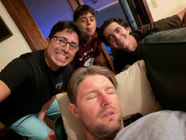 Three men and a boy posing for a selfie behind a man sleeping on a couch.