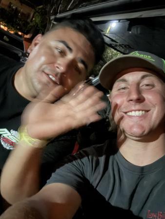Two men smiling at the camera, one waving his hand in the foreground.