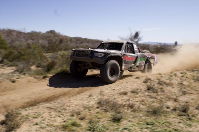 A dusty trophy truck speeding across a desert dirt track.