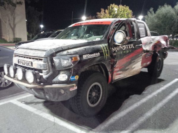 A muddy Toyota Tundra off-road truck with Monster Energy decals parked in a parking lot at night.