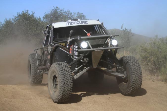 A Moncure off-road racing truck kicking up dust on a dirt trail.