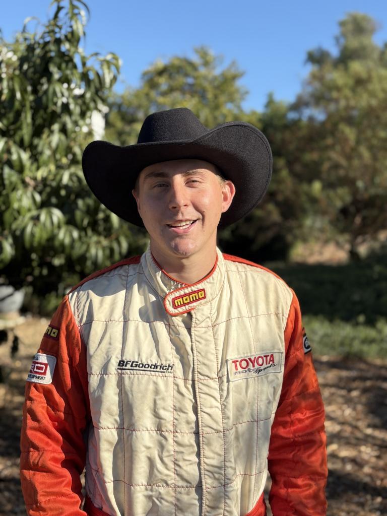 A man wearing a black cowboy hat and an orange and white Toyota racing suit.