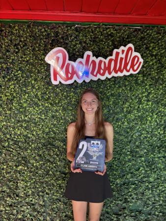 A smiling woman holds a blue award plaque in front of a green wall with a Rochodile sign.