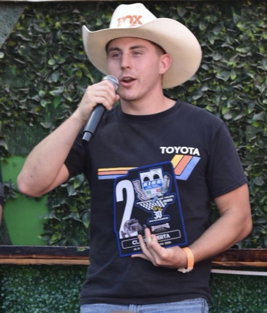Contact Long Beach Racers: Jack Moncure, driver wearing a cowboy hat and a black Toyota t-shirt speaks into a microphone while holding a racing trophy.