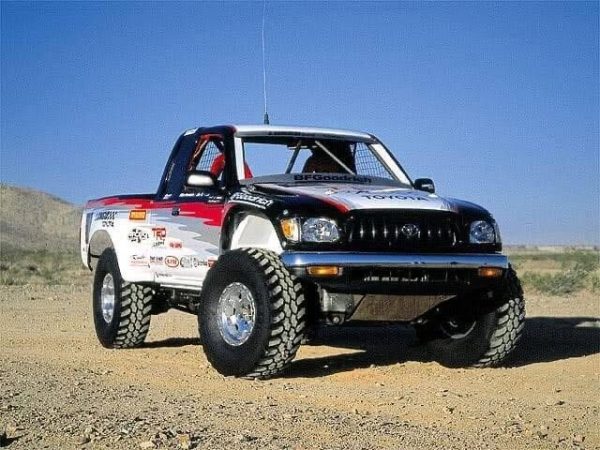 Toyota trophy truck with red, white, and black racing livery on a dirt desert track.