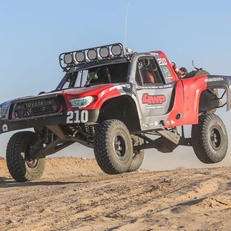 A red and grey Toyota trophy truck numbered 210 jumps over a dirt mound.