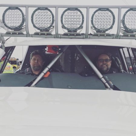 Two men sitting in the cab of an off-road vehicle with a light bar mounted on the roof.