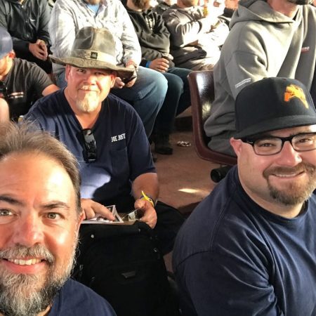 Three men smiling while sitting in an audience.