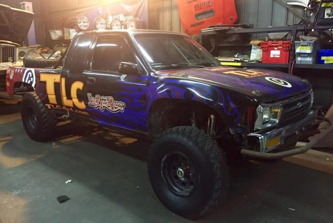 A Toyota pickup truck in a garage, featuring a black and purple flame paint job and TLC branding on the side.