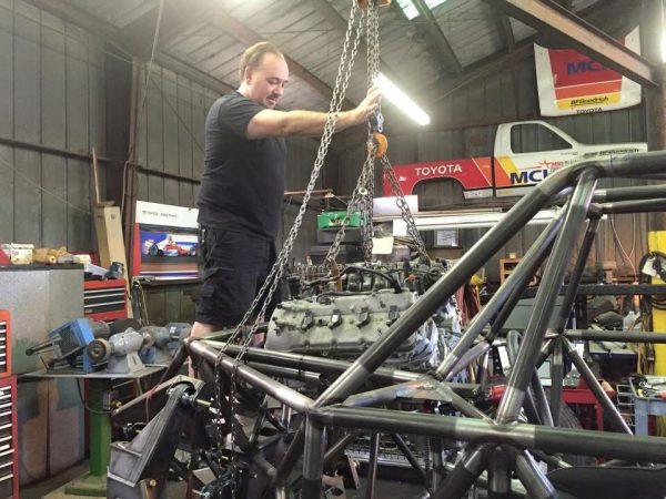 A mechanic uses a ceiling hoist to lower an engine into the chassis of a race car.