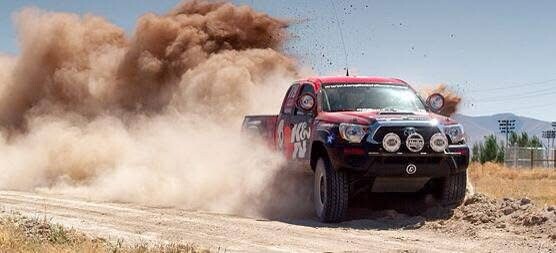 A red off-road racing truck kicking up a large cloud of dust while driving on a dirt track.