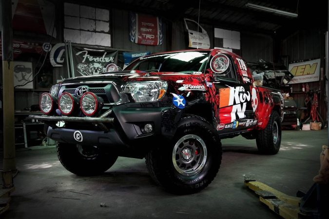 A customized Toyota Tacoma off-road truck with a red and black K&N racing livery parked inside a workshop.