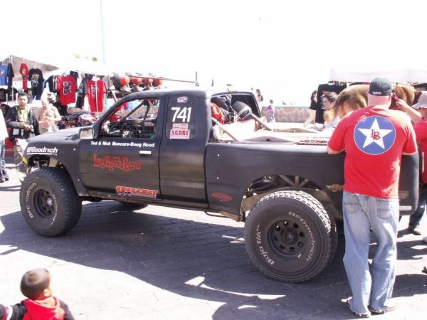 A black off-road racing truck with the number 741, displayed at an outdoor event, with spectators standing nearby.