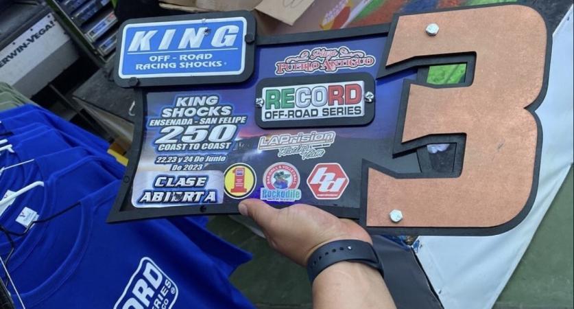A hand holds a trophy plaque for the King Shocks 250 off-road race, featuring logos for the Record Off-Road Series, race dates of June 22-24, 2023, and a large copper-colored number three.
