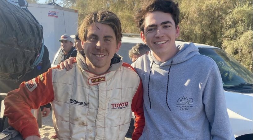 Jack Moncure and Jacob Hunter smiling while posing for a photo outdoors, one wearing a Toyota racing suit and the other in a gray hooded sweatshirt.