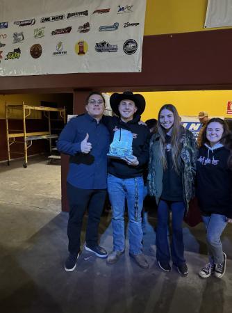 Four young adults posing for a photo, with the person in the center holding a championship trophy.