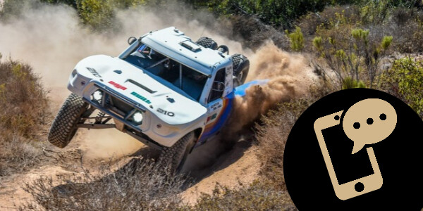 Long Beach Racers- A white off-road racing truck kicks up dust while driving through a dirt path.